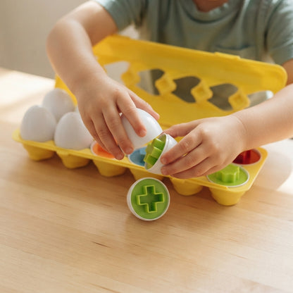 Child hands fitting two coloured shape egg halves together above the carton